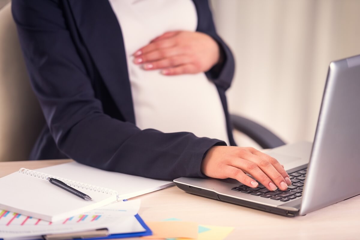Delaware paid family leave: pregnant employee using a laptop while holding her belly
