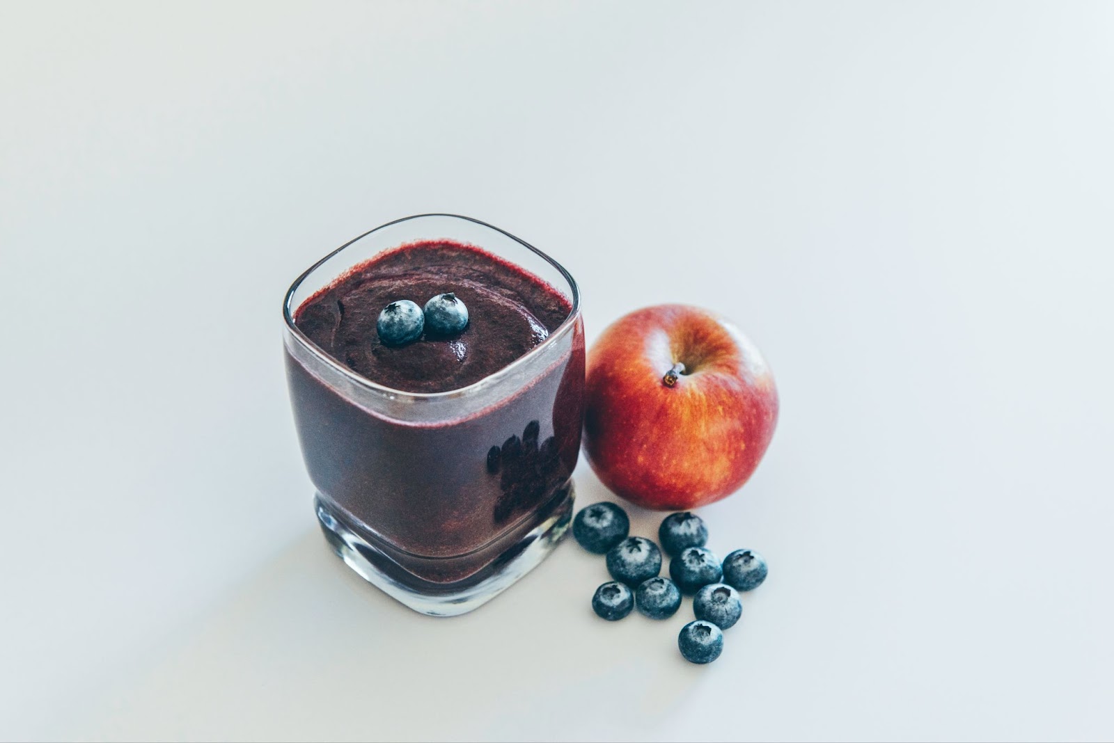 an apple and blueberries beside a glass of smoothie