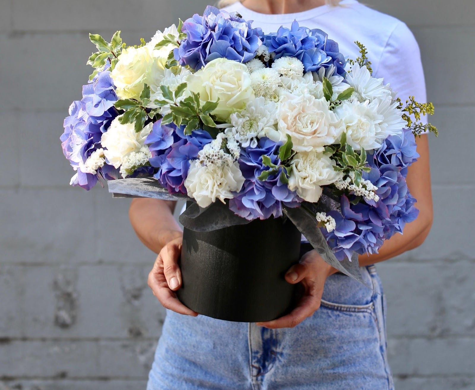 An elegant box arrangement filled with blue hydrangeas, white roses, chrysanthemums, and assorted greens, creating a charming and artistic floral display.