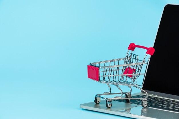 Online shopping , a shopping cart placed alongside a notebook on a blue .