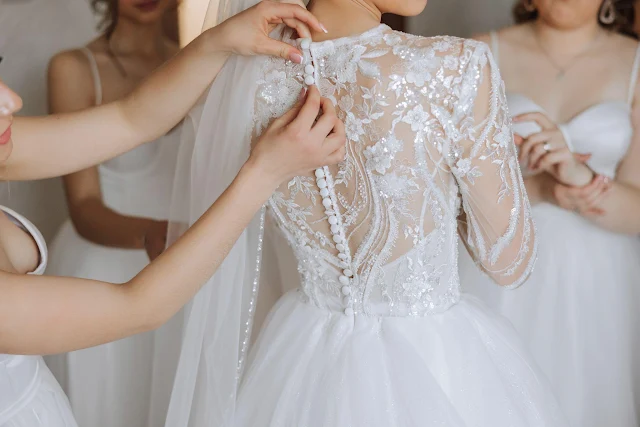 Several bridesmaids helping the bride try on a wedding dress
