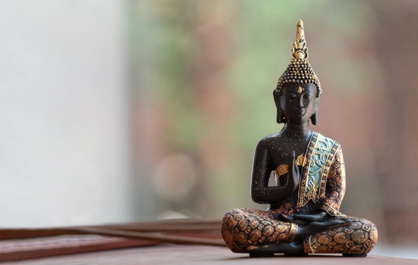 A statue of a buddha sitting on a table  Description automatically generated