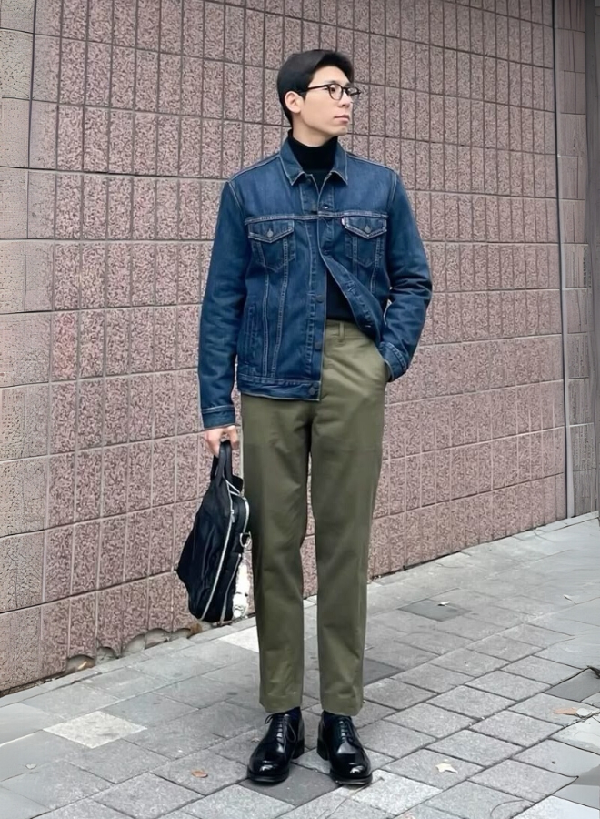 Pria mengenakan jaket denim, turtleneck hitam, dan celana olive.