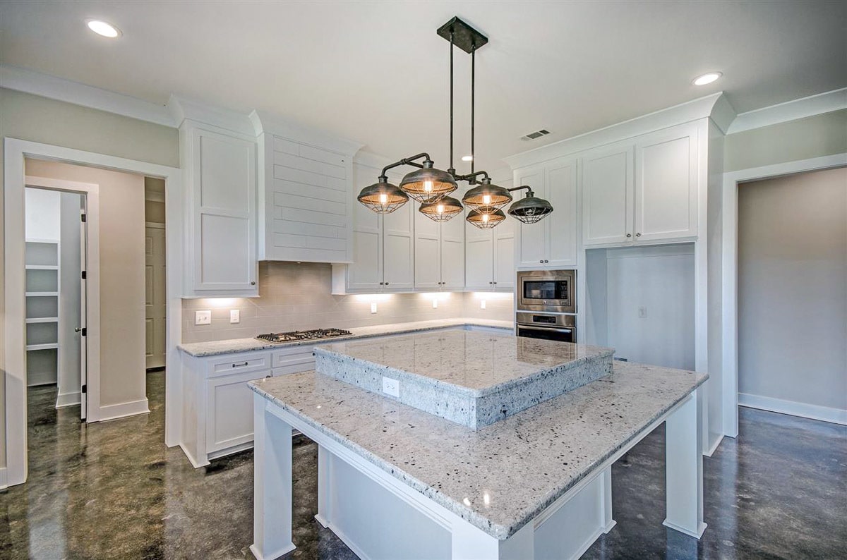 The kitchen is equipped with a double wall oven. built-in cooktop, white cabinetry, and a raised center island.