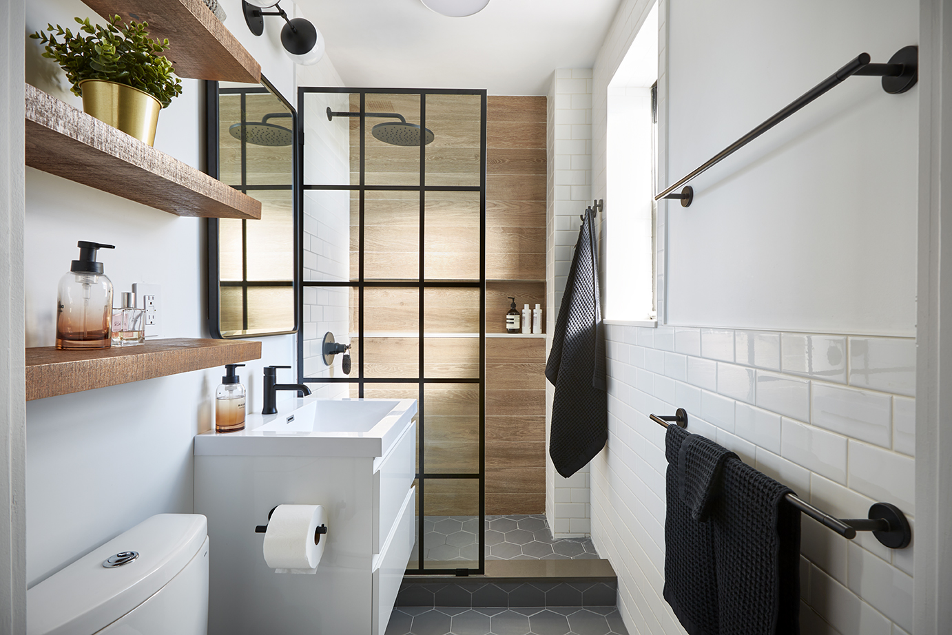 3/4 bath with walk in framed shower, wood grain wall tile, a white floating vanity, gray hexagonal floor tiles, floating wall shelves, and matte black fixtures and hardware