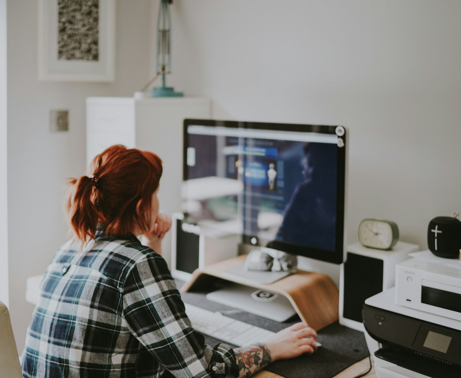 A person with red hair working on a desktop computer in a home office environment, highlighting the importance of maintaining a secure and organized workspace to protect computer data.