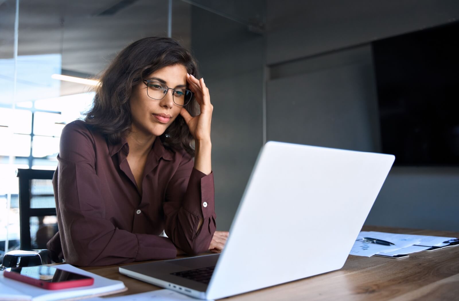 Woman wearing glasses, experiencing digital eye strain while working on a laptop, highlighting the impact of screen time on eye health.