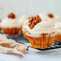 A carrot cake cupcake with cream cheese frosting topped with a walnut.