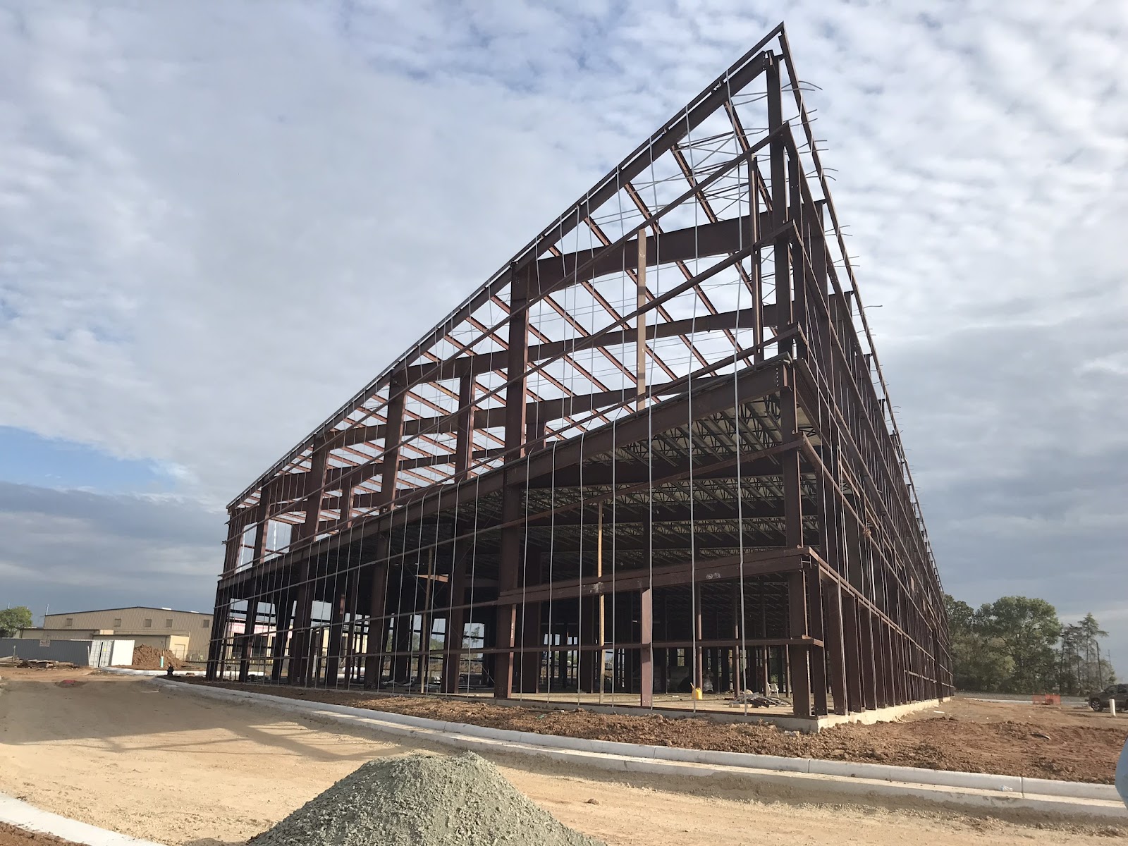 A large industrial building under construction, showcasing its exposed steel framework against a partly cloudy sky.