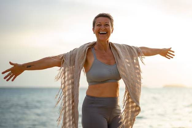 Joyful mature woman stretching by the ocean at sunrise, radiating confidence and vitality
