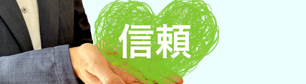 スーツ姿の人物が「信頼」と書かれた緑色のハートを両手で持っている