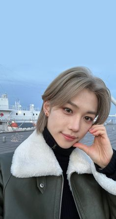 This  contain Felix with grey hair wearing a black turtle neck sweater and green leather jacket standing in front of a large ship