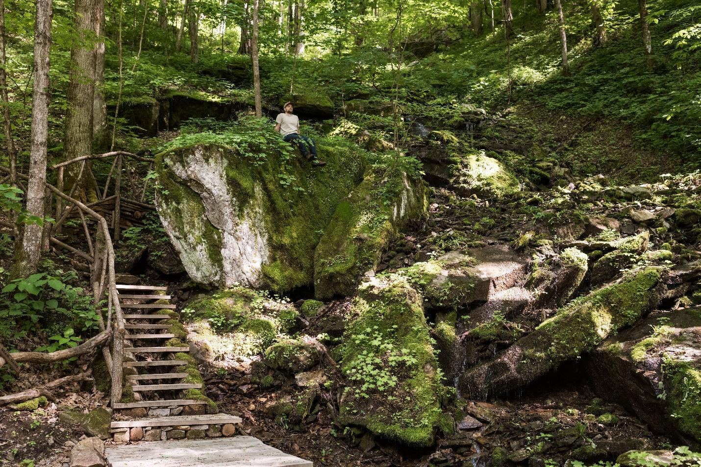 A person sitting on ancient boulders next to waterfall and hiking trail.