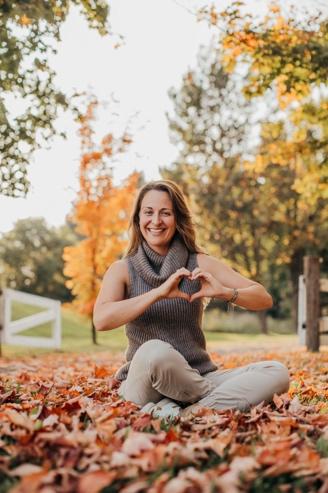 A person sitting on the ground making a heart with her hands

Description automatically generated