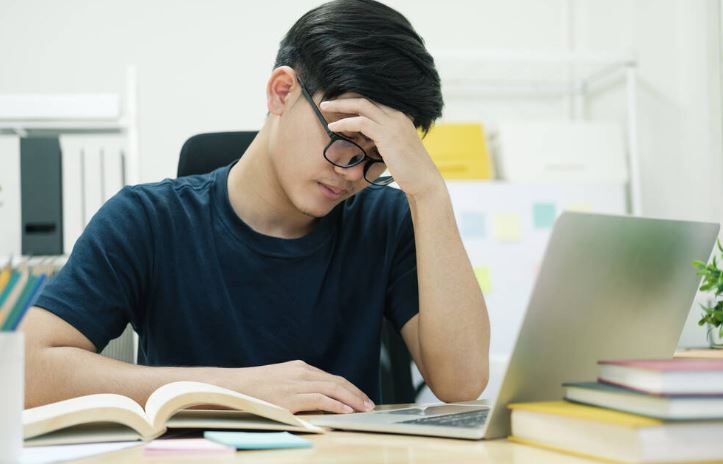 Tired exhausted young man massaging nose bridge, taking off glasses, feeling eyestrain, sitting at work desk,