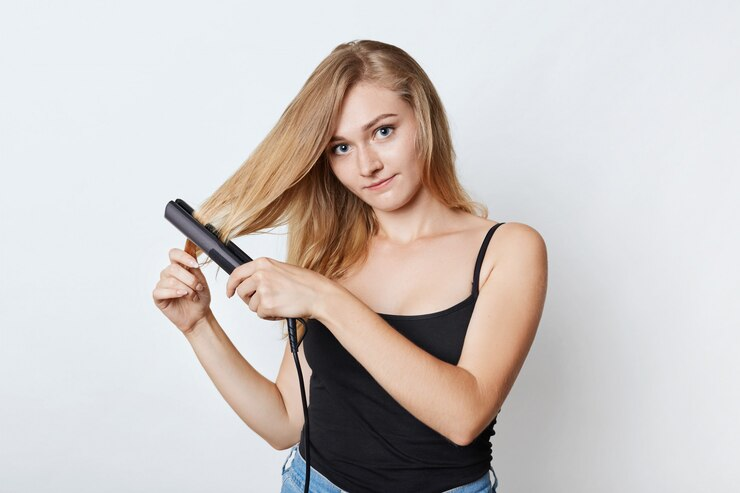 Pretty woman styling her hair with straightener