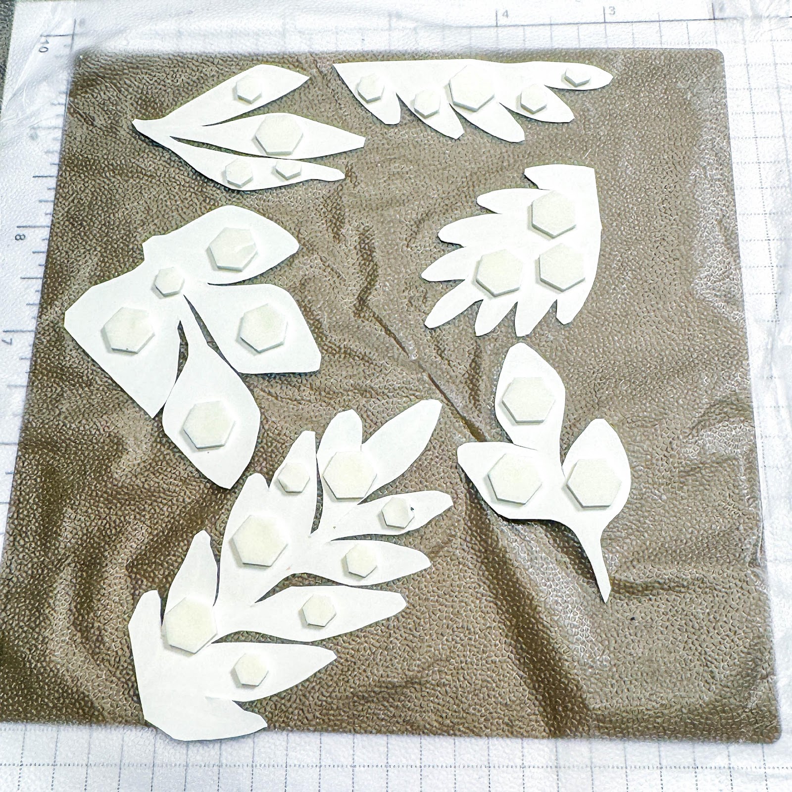 A white paper cut out of leaves on a brown surface

Description automatically generated