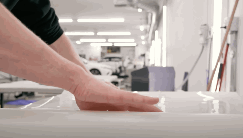 A technician runs their hand over a freshly wrapped car panel in a well-lit workshop, checking for imperfections in the protective film