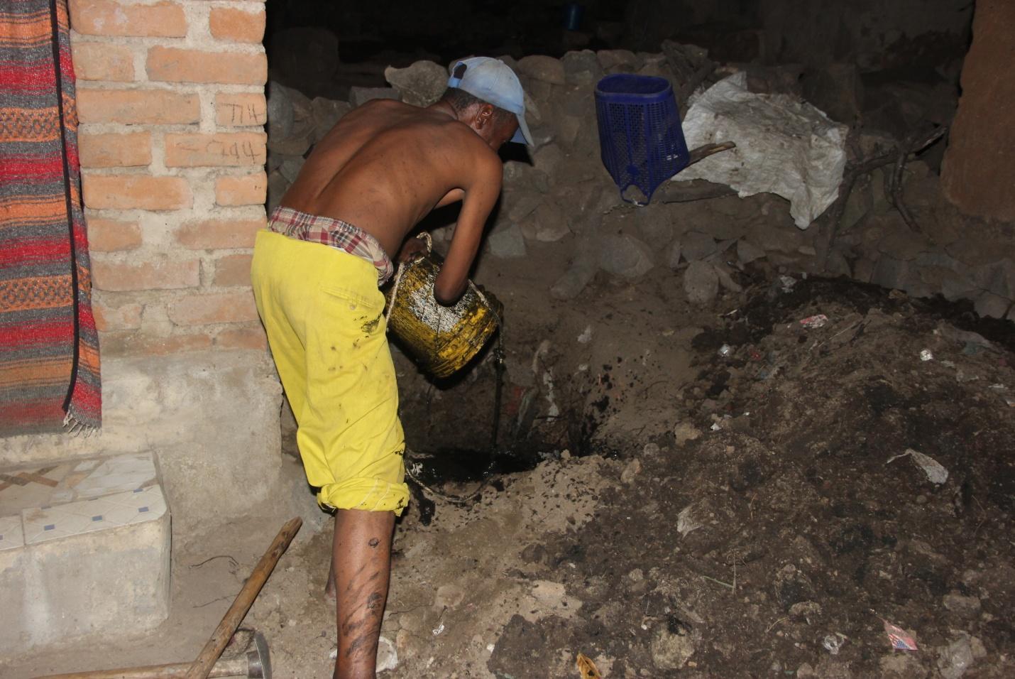 A toilet emptying assistant discharging the faecal sludge just behind the wall of the yard, in a public street