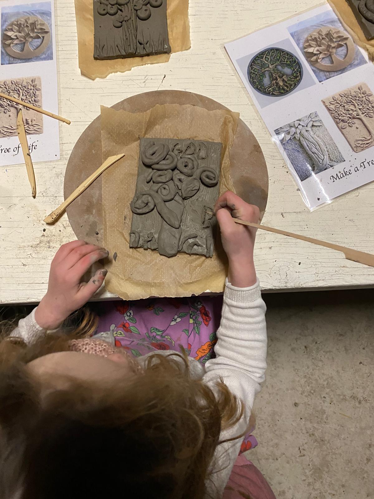 A child working on a clay tile, creating a tree with a stick.