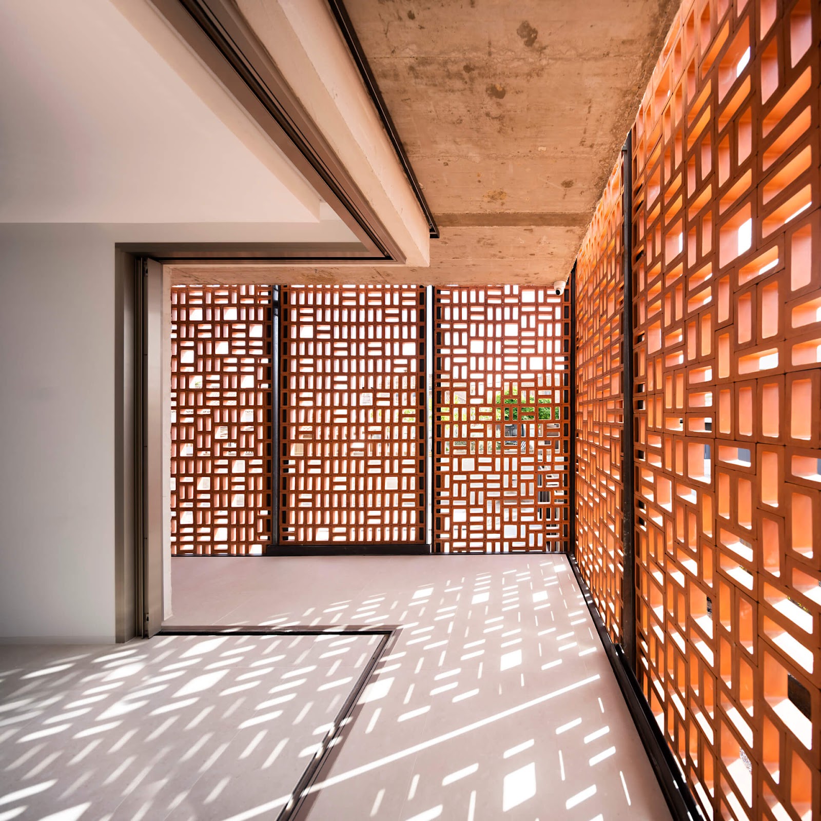 A modern interior space with large windows featuring a geometric lattice design jali, allowing sunlight to create intricate shadow patterns on the floor.