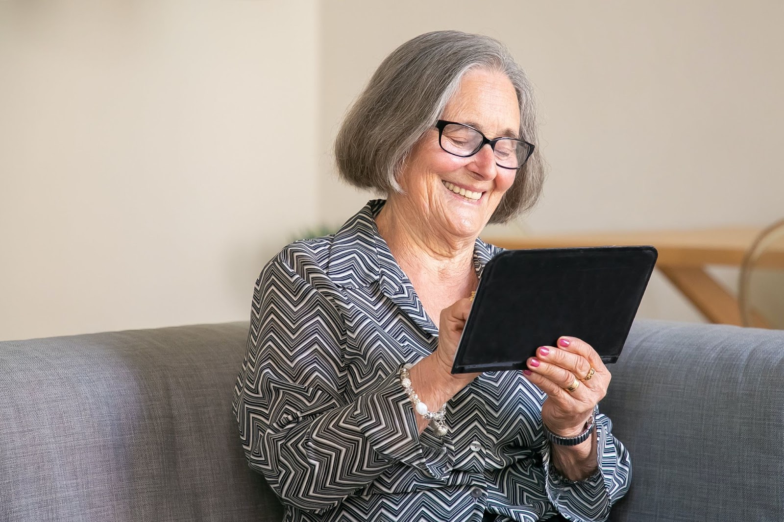 An elderly woman smiling at looking at a digital tablet