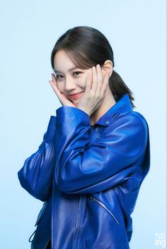 This contains an image of Hyeri on a blue jacket with her hands on her face