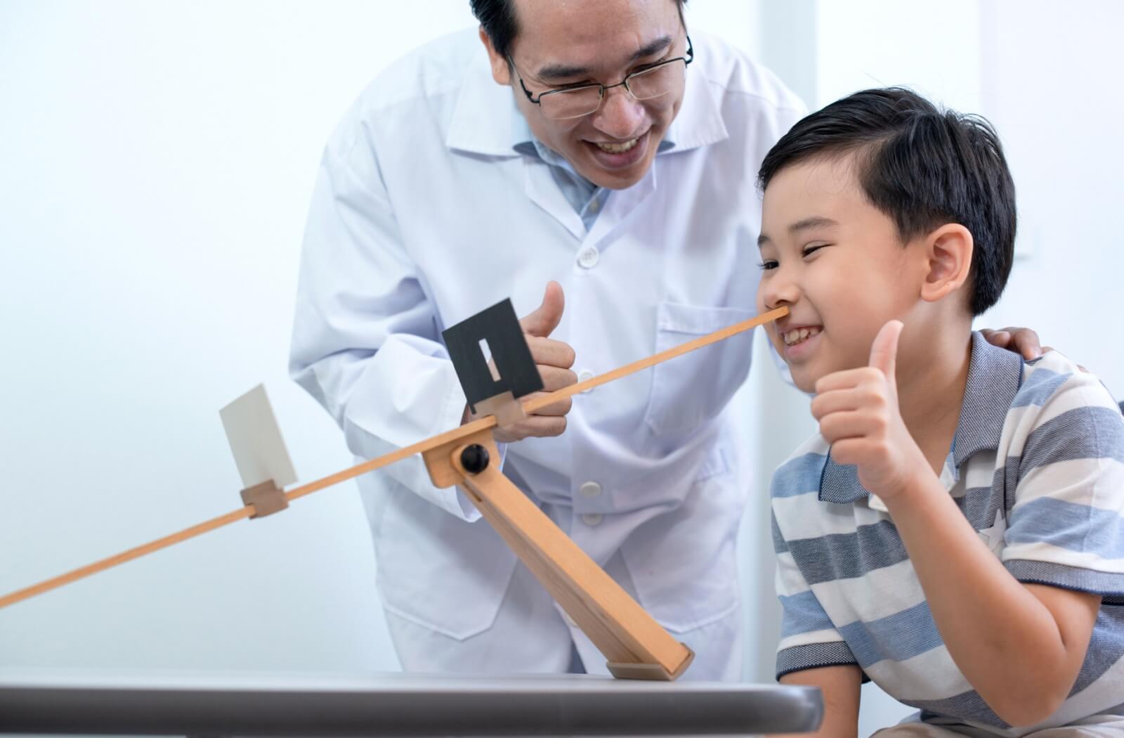 A young child enthusiastically performs eye exercises under the guidance of an eye doctor during a vision therapy session.