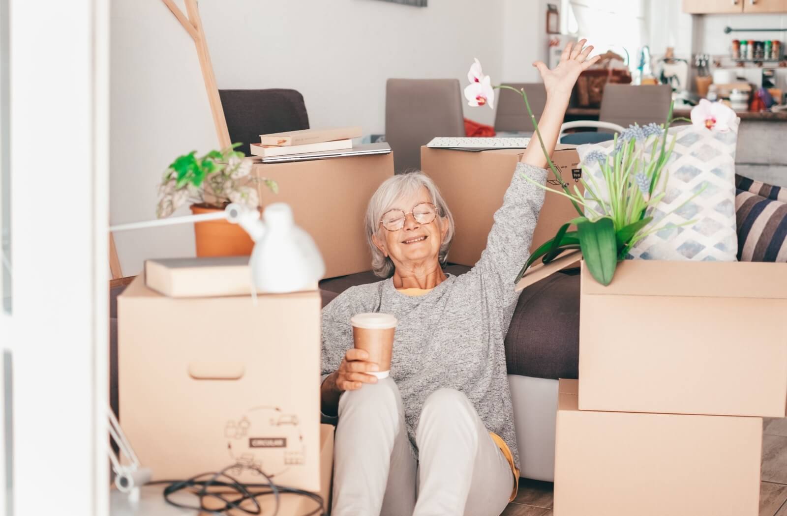 A happy senior sits on the floor, surrounded by boxes of all their treasured possessions in prep to move into memory care