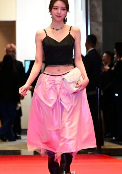 This contains an image of ITZY Yuna on a  black cropped tank top and a pink skirt looking beautiful and a black boots