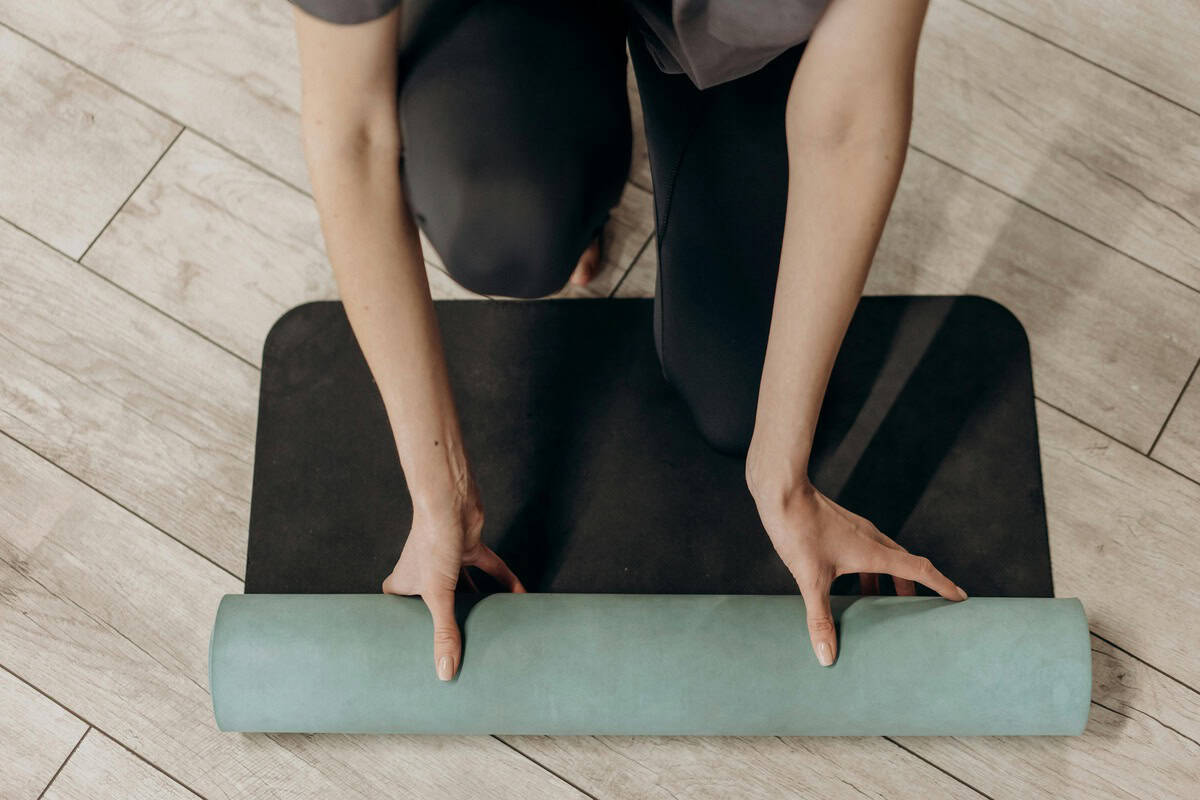 Foto de uma mulher abrindo um tapete de yoga em um estúdio, mostrando apenas as mãos e braços e uma parte das pernas da mulher dando ênfase no tapete de yoga.