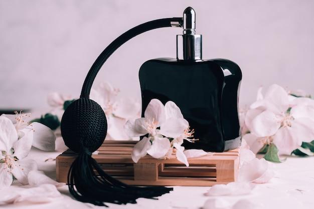 Black bottle eau de toilette or perfume with long tassel spray pomp, on wooden podium in form of pallet on light plaster surface with apple flowers