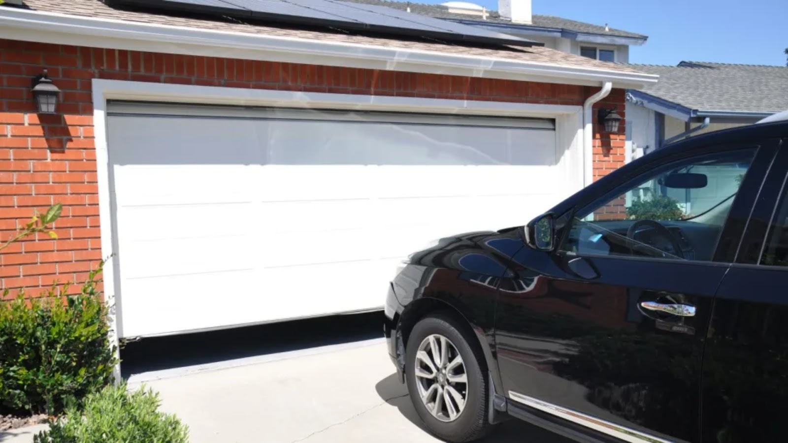A black car parked in front of a white sectional garage door