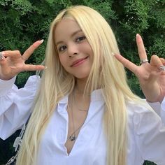 This contains an image of sorn with long blonde hair holding two fingers up in front of her face and making the peace sign