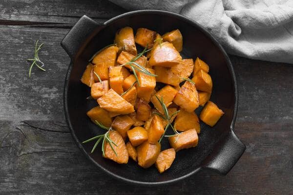Roasted sweet potato chunks garnished with rosemary sprigs, served in a black bowl on a rustic wooden