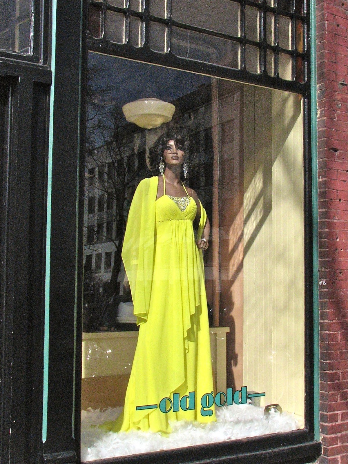 Photo of the Old Gold storefront with a view of a mannequin wearing a yellow dress in the window display