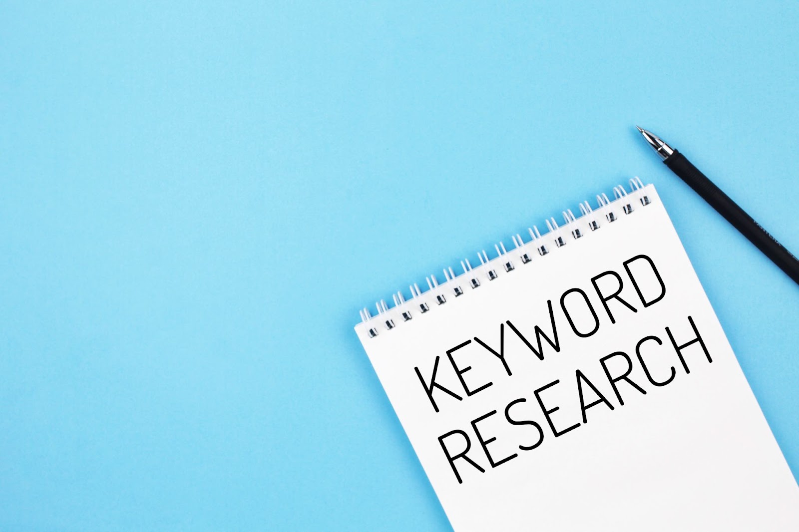 Words “KEYWORD RESEARCH” written on a piece of paper next to a pen. 