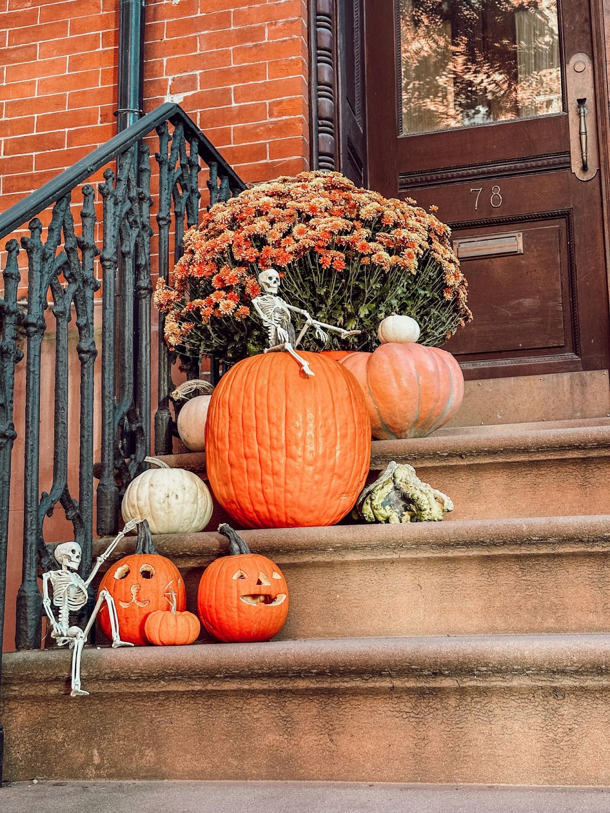 Front steps of a townhome decorated with orange pumpkins, orange mum flowers, small gourds, and small skeletons