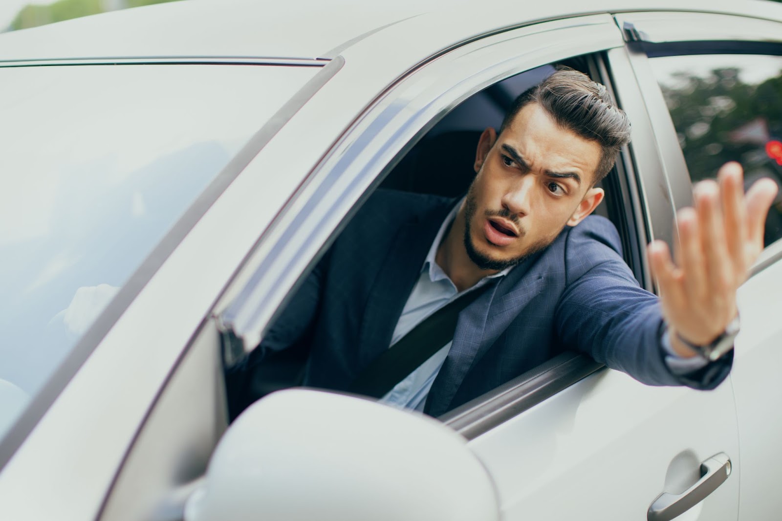 A man in a suit driving a car and waving his hand