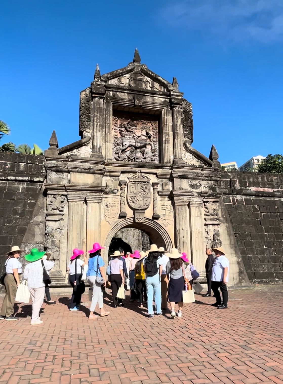 A group of people walking in front of a stone buildingDescription automatically generated