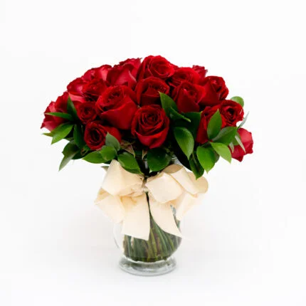 Arranjo de rosas vermelhas em vaso transparente com laço branco.