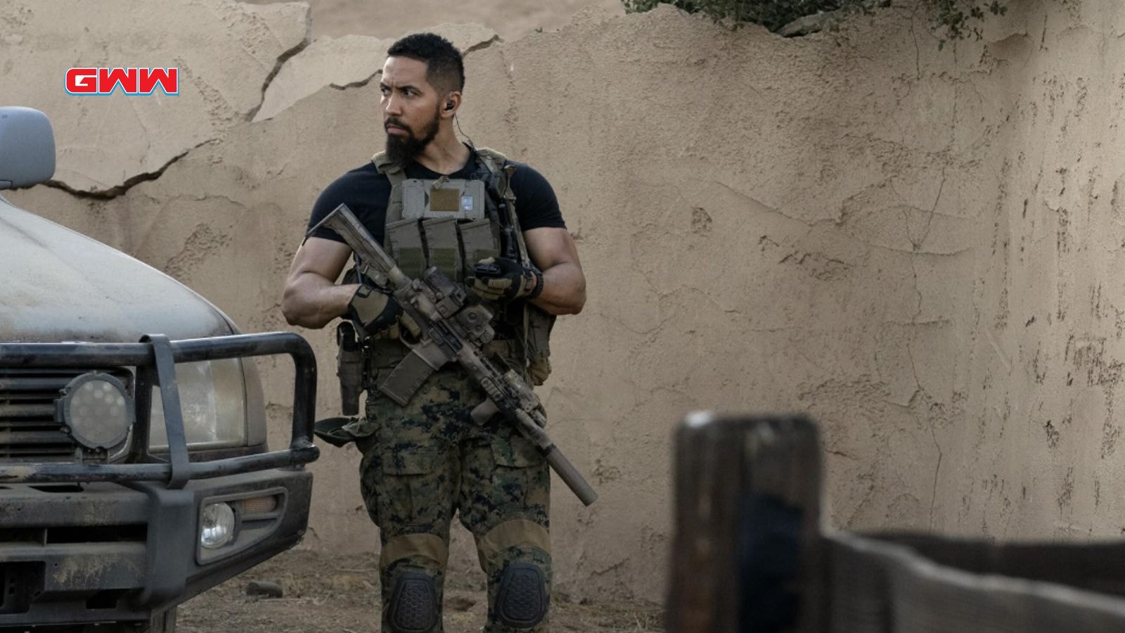 Raymond stands alert beside a vehicle, prepared for action.