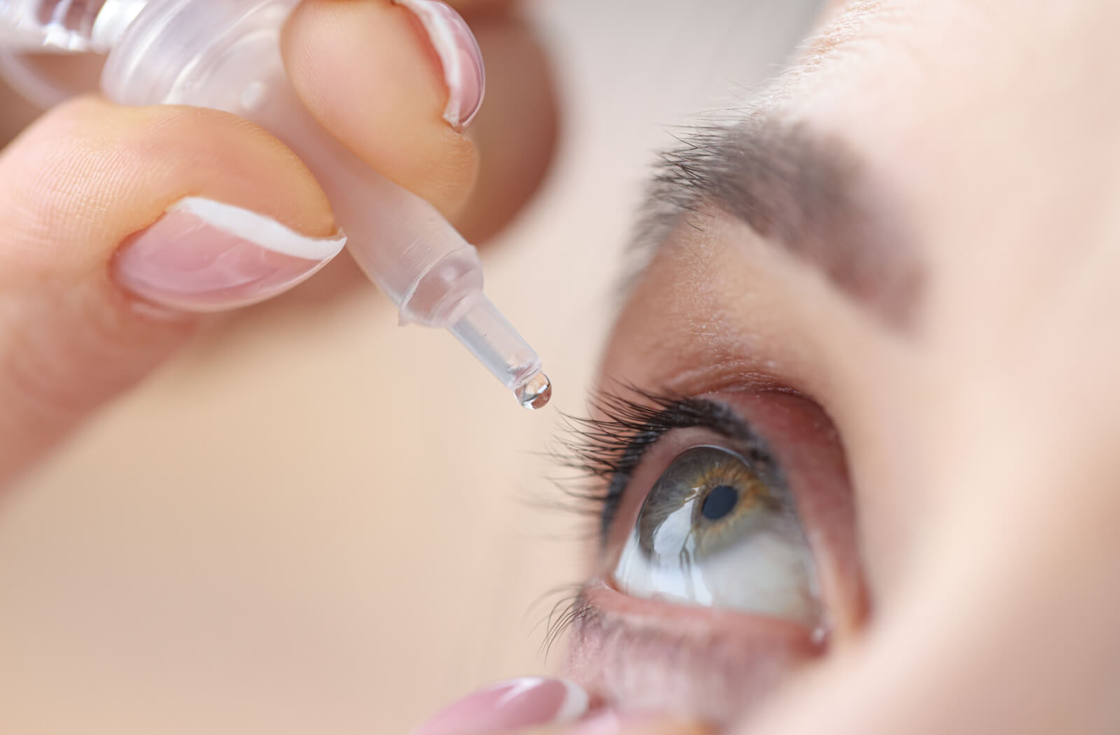 A close-up of one of a person's eyes as they apply artificial tears out of a squeeze bottle.