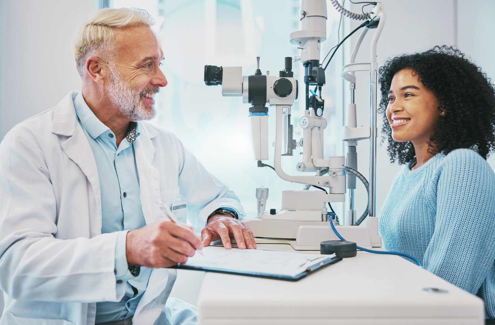 An optometrist smiling across the table at his patient while discussing the results of her eye exam.