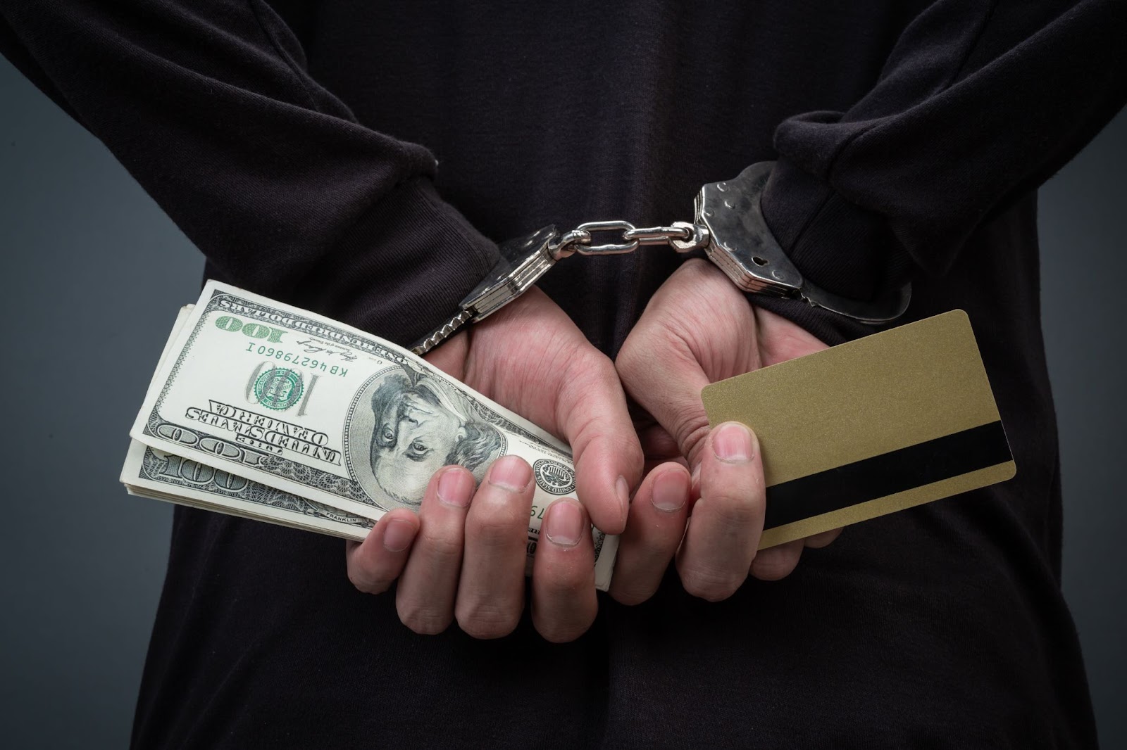 Handcuffed hands holding cash and a credit card, symbolizing arrest