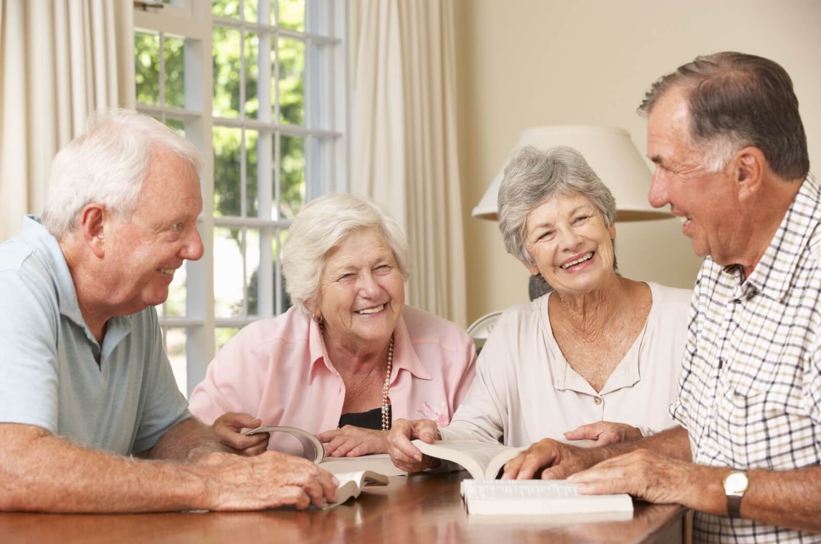 A group of smiling older adults sitting at a table with open books having a discussion.