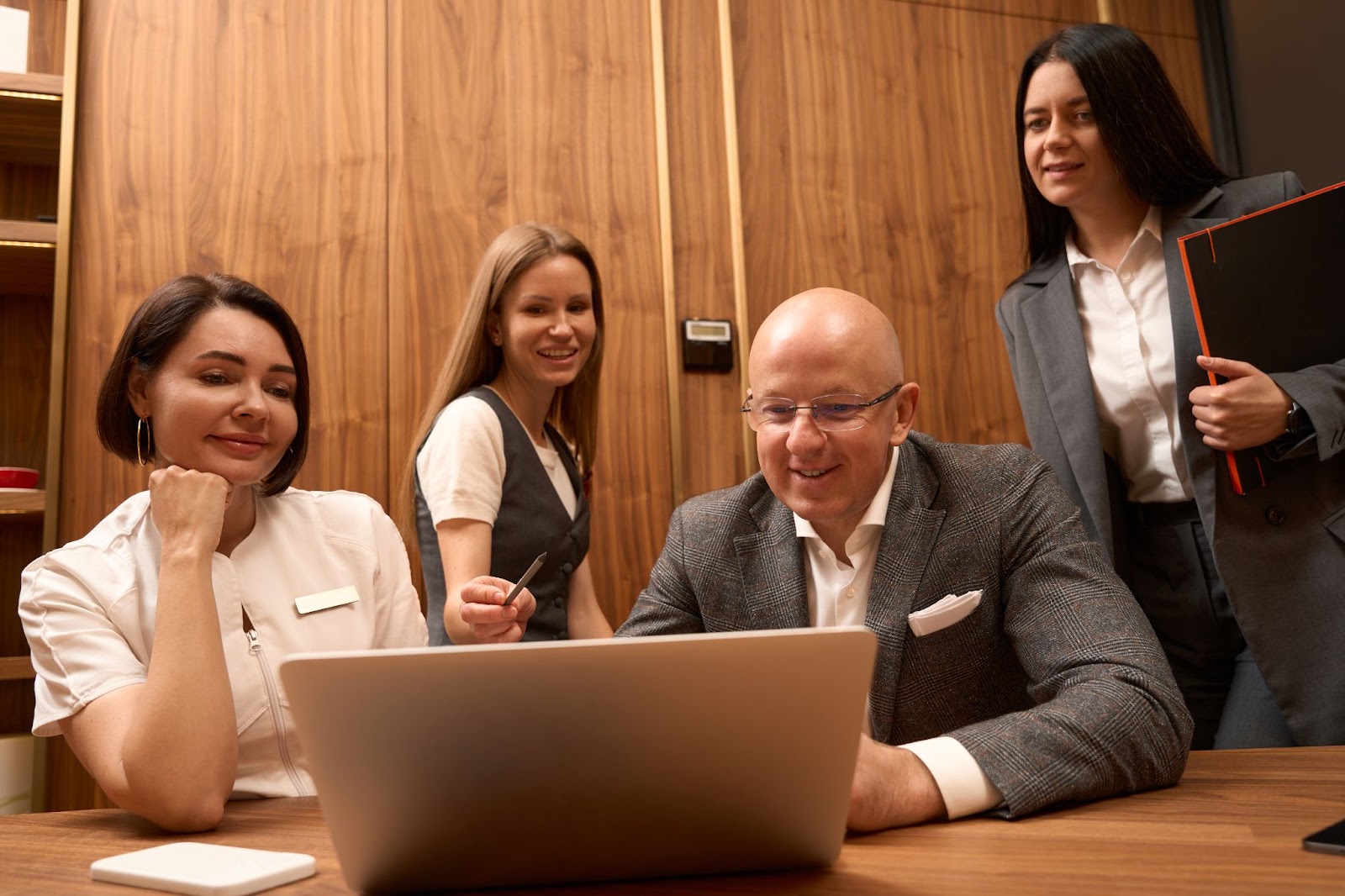  Three entrepreneurs collaborate on business registration requirements, and a young woman seated behind them points at the laptop screen while guiding the group.