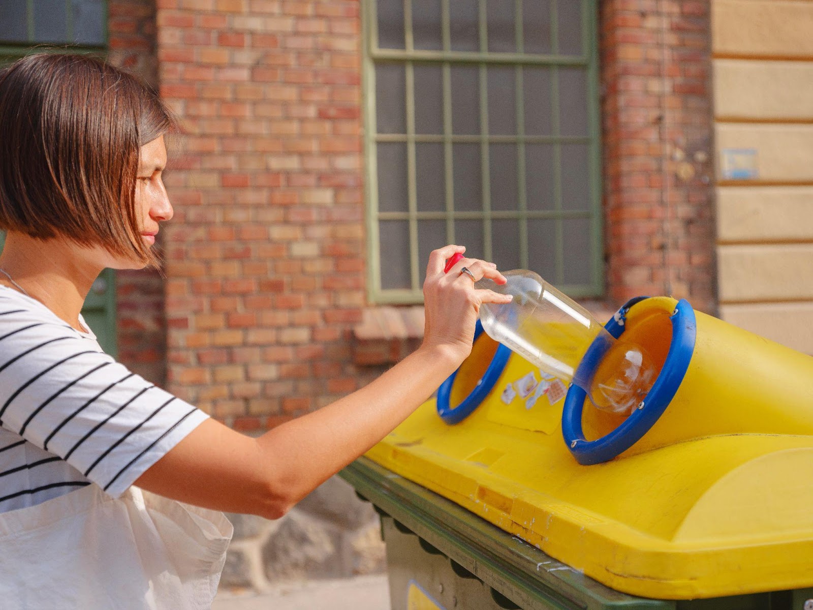 person putting a plastic bottle into a recycling container