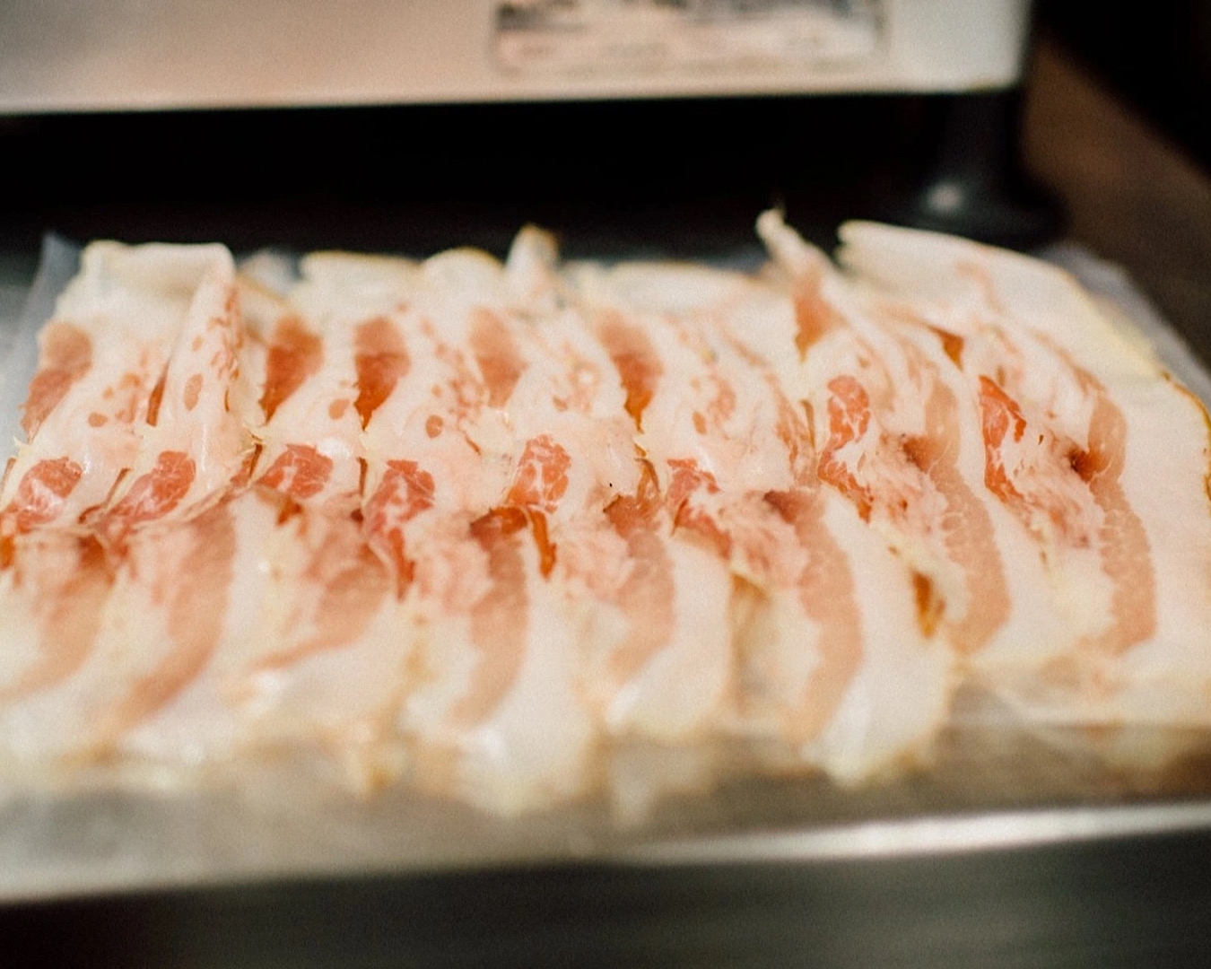 Quality, uncooked bacon lines a baking sheet covered baking tray.