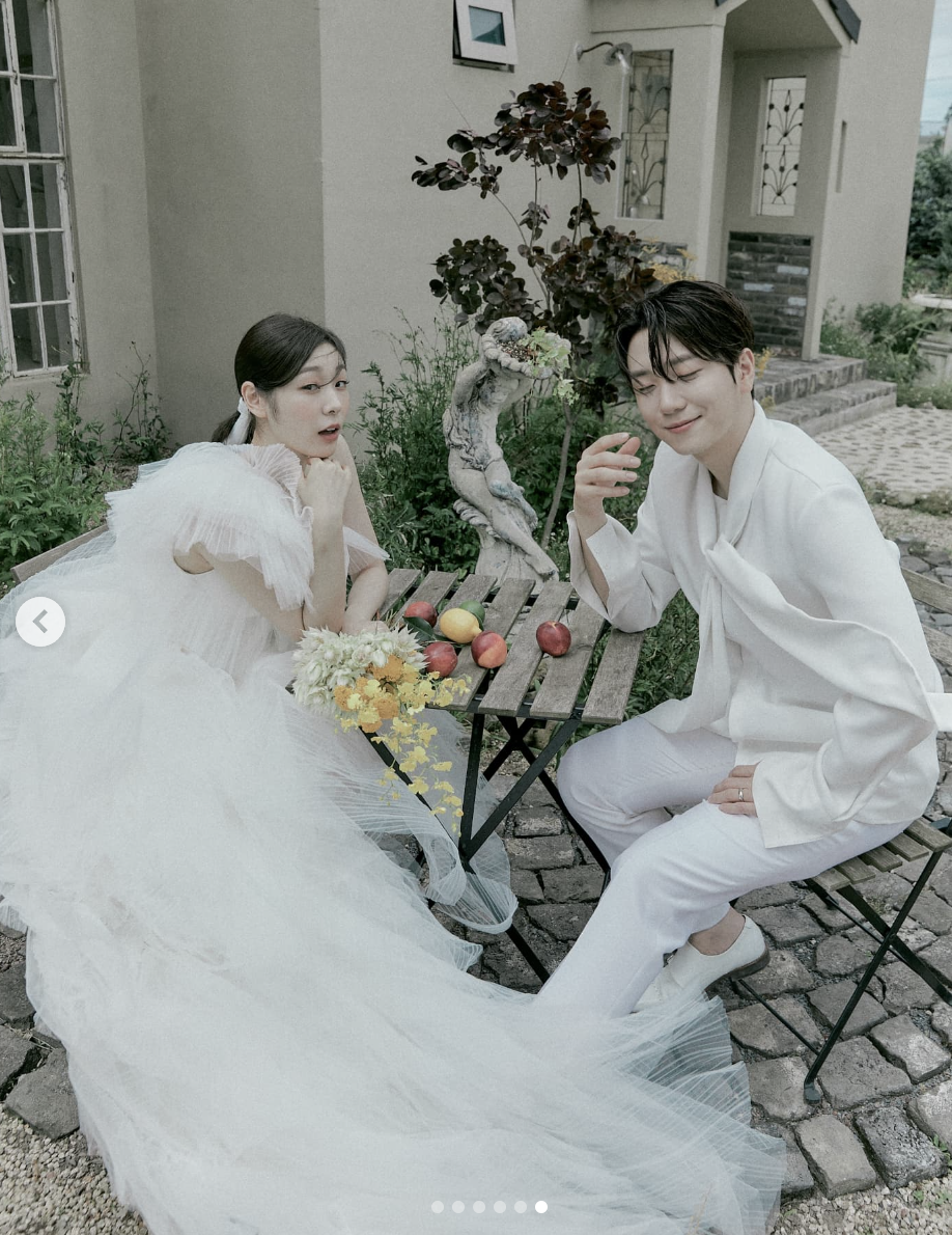 A wedding picture of Kim Yuna and her husband Ko Woo Rim sitting on a table with fruits on the table 